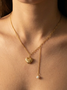 Détail d'un pendentif cœur doré et d'une perle blanche sur une chaîne en Y élégante