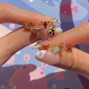 Golden sea animal stud earrings set with colorful zircons shown on fingertips