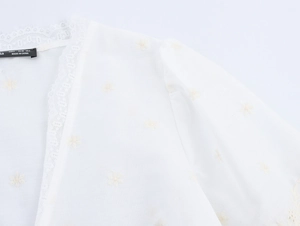 Détail de broderie florale et bordure en dentelle sur ce chemisier blanc à col en V