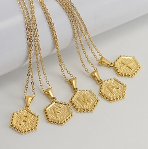 Detail view of 18K gold plated hexagon pendants with engraved letters P, F, M, A, and X