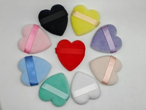 Colorful heart-shaped powder puffs with ribbon handles arranged on a white background
