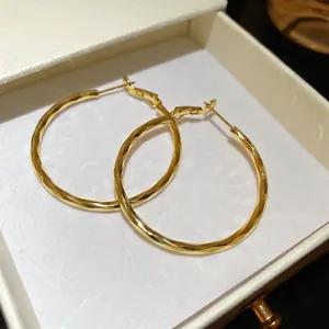 Pair of twisted 14k gold plated round hoop earrings displayed in a beige jewelry box