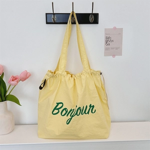 Detailed view of light yellow canvas tote bag with green Bonjour print and drawstring closure