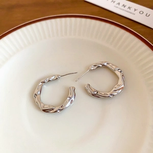 Detail of silver wave hoop earrings with inlaid zircons on a rustic ceramic plate