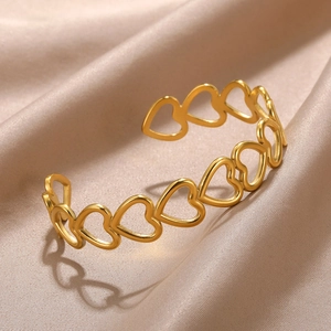 Detail view of heart-shaped hollow gold open cuff bracelet on elegant silk background