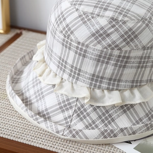Detailed view of plaid fabric texture and ruffle edge on a beige sun hat for women