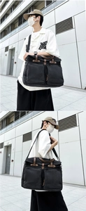 Detail view of large capacity black canvas messenger bag with dual front pockets and leather straps