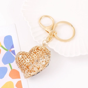 Detail of gold-colored hollow heart keychain with floral engraving and crystal accents