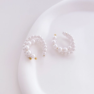 Macro shot of elegant white pearl C-shaped hoop earrings on a ceramic dish