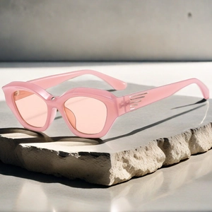 Detail of pink jelly Y2K cat-eye sunglasses with silver metal wing accents on stone