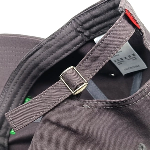 Detail of adjustable metal buckle on dark brown cotton baseball cap with wash label