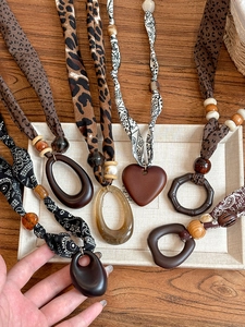 Ethnic fabric scarf necklaces with wooden pendants displayed on a rustic tray