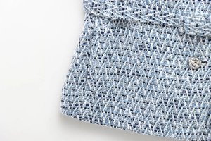 Detailed close-up of blue and white tweed fabric texture with decorative metal buttons