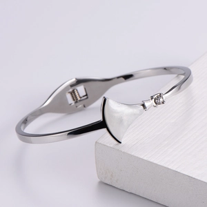 Detailed close-up of a silver stainless steel bangle with white shell fan charm on stone
