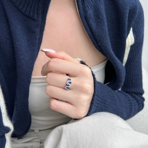 Detailed view of an S-shaped wave silver ring with blue gemstone on a finger