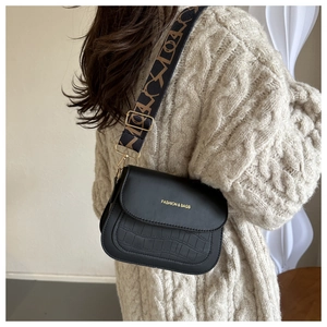 Detail of black crossbody saddle bag with crocodile texture and patterned wide strap