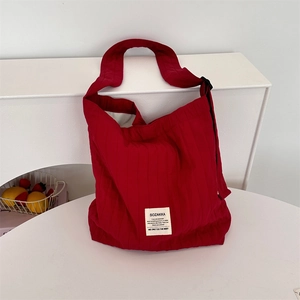 Detail of red quilted canvas shoulder bag with black strap adjuster on white table