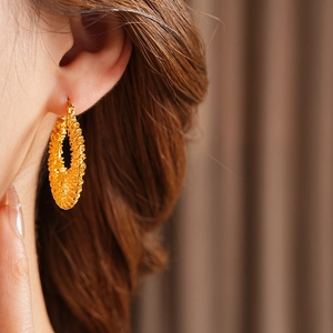 Gros plan de boucles d'oreilles créoles tressées plaquées or portées par un mannequin
