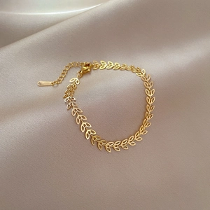 Detail of gold titanium steel clover leaf chain bracelet on elegant champagne silk fabric
