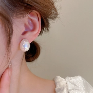 Gros plan de boucles d'oreilles ovales minimalistes aux reflets nacrés sur modèle