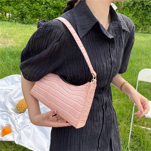 Pink crocodile pattern leather underarm bag held by model on outdoor grass background