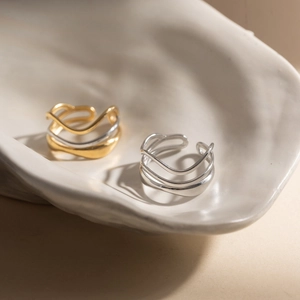 Modern 18K gold and silver plated stainless steel wavy open rings set on ceramic tray