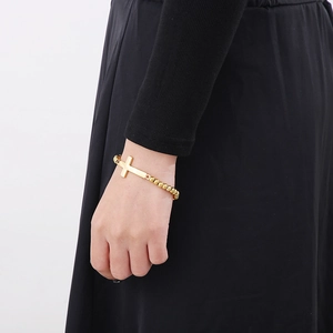 Détail d'un bracelet à billes doré avec un pendentif croix horizontale minimaliste