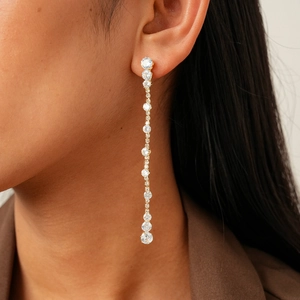 Detail of long gold-plated drop earrings with sparkling round zircon tassels on model