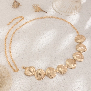 Detailed close-up of golden seashell-shaped body chain on a sandy beach setting