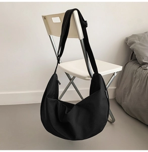 Close-up of black nylon crescent bag with adjustable strap on white chair