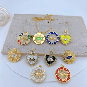 Gold-plated Evil Eye and heart pendants with zircon inlay on a textured stone surface