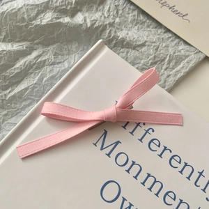 Elegant pink ribbon bow hair clip for women on a minimalist textured background