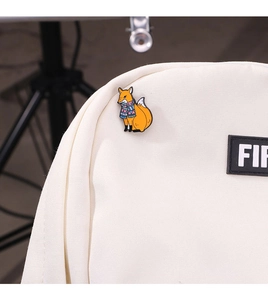 Detailed view of an orange fox enamel pin with a scarf attached to a canvas backpack