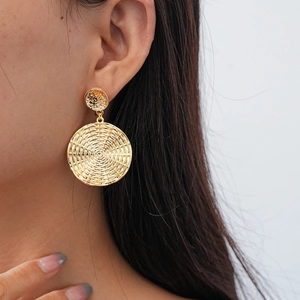 Close-up of gold geometric round earrings with woven texture worn by a model