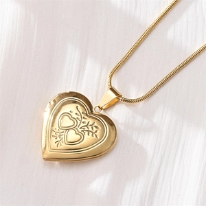 Close-up of golden heart locket necklace with floral engraving on white textured fabric