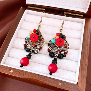 Macro shot of vintage dragonfly earrings with red rose charms and colorful beads in a box