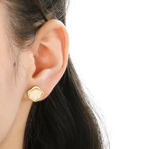 Detail view of a gold flower earring with white shell inlay worn by a female model