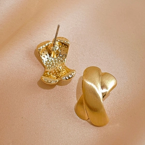 Detailed macro view of gold cross stud earrings with brushed metallic texture on silk