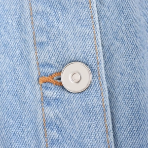 Detail of light blue denim fabric with orange contrast stitching and silver metal button