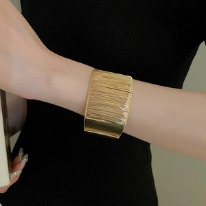 Macro shot of gold wide cuff bracelet showing brushed metal texture and geometric style