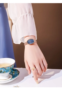 Detail of rose gold oval watch with blue mother of pearl dial and mesh strap on wrist