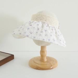 Détail du tissu matelassé à fleurs mauves et bordure en dentelle beige sur le chapeau