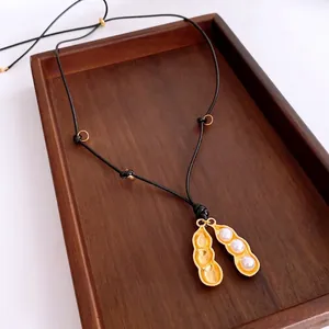 Elegante collana con ciondolo arachide dorata e perle bianche su cordino nero