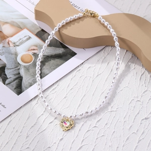 Close-up of a hollow gold heart pendant with iridescent gemstone on a pearl necklace