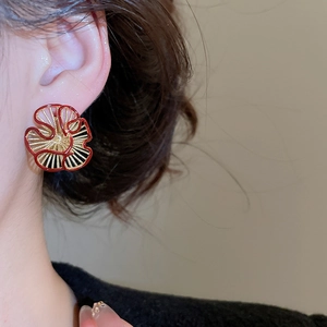 Close-up of red and gold floral earrings with radiant petals on a model's ear