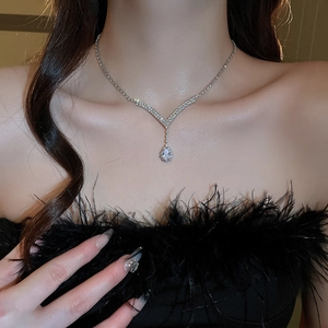 Detail of silver V-shaped necklace with rhinestones and pear-shaped pendant on model