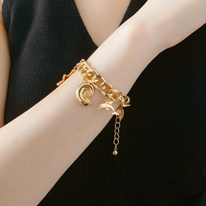 Close-up of golden chunky chain bracelet with seashell and dolphin charms on wrist