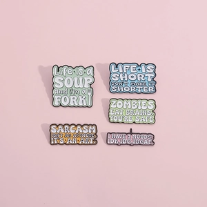 Detailed view of colorful enamel pins with humorous slogans on a soft pink background