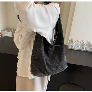 Detail of a large dark grey denim tote bag being carried by a model in a natural setting