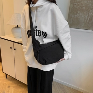 Minimalist black nylon crescent tote bag shown on model in a modern interior setting